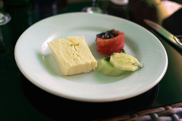 Saluguni cheese, tomato and cucumber in a white plate on a table in a restaurant. Vegetarian food