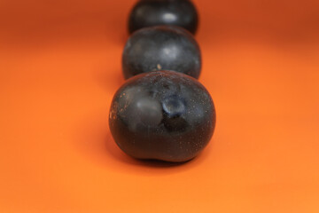 Plum close-up on a uniform orange background. Healthy vegetarian food in summer