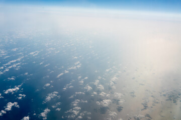 View of the clouds in the sky outside the plane window while flying high above the blue sea