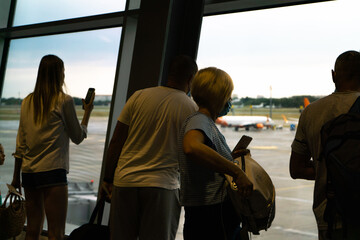 Tourists look at the runway of the airfield through a large window in the early morning of a summer day
