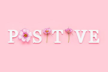 Positive. Motivational quote from white letters and beauty natural flowers on pink background. Creative concept inspirational quote of the day