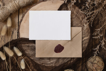 Blank paper card on sealed envelope and wooden table with dried plants