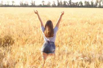 Naklejka na ściany i meble Beautiful young happy girl with a dry wheat field, stands with her back