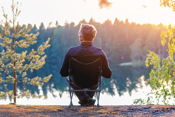 A man sits in a folding chair at sunset outdoor. - obrazy, fototapety, plakaty