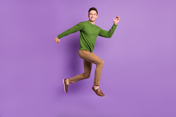 Full length profile photo of young brunet guy jump wear sweater trousers sneakers isolated on purple background