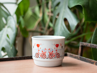 Mid-century modern porcelain mug with bicycle pattern on a wooden table with tearing palm in the background