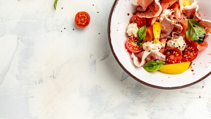 White bowl of fresh and healthy Mediterranean salad with tomatoes, cream cheese balls, prosciutto jamon and basil leaves. Delicious balanced food concept. Long banner format. top view