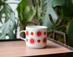 Mid-century modern porcelain mug with red dot pattern on a wooden table with tearing palm in the background