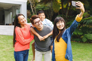 Happy asian parents, son and daughter smiling outdoors and taking selfie in garden