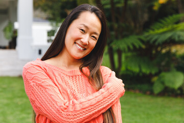 Portrait of happy asian woman smiling in garden outside family home wearing pink sweater