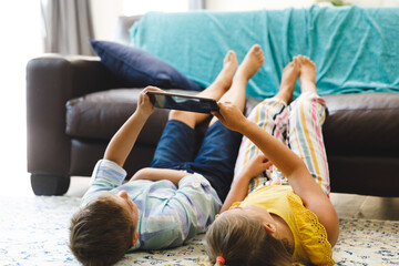 Caucasian brother and sister lying on living room floor using tablet