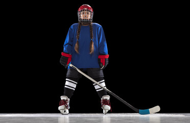 Full-length portrait of young girl playing hockey isolated over black background