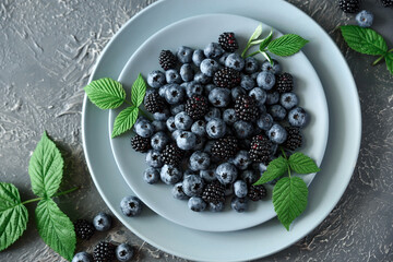 Fresh blueberries and blackberries decorated green leaves on gray concrete background. Top view