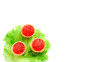 Three tartlets with red caviar lying on lettuce leaf on white background. Copy space. Top view.