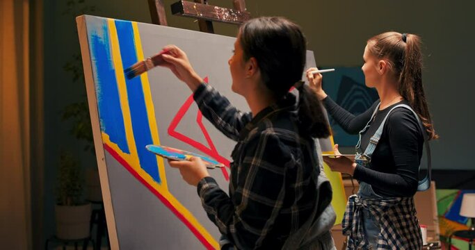 Artists in dungarees and checked shirts create a new modern abstract painting using acrylic paints paint on a large canvas, standing on two sides, blue stripes, yellow dots, color combinations