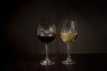 A glass of red and a glass of white wine. Reflection of the restaurant in the glasses. Dark background.