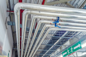Metal pipes mounted under the ceiling are covered with thermal insulation at a modern production...