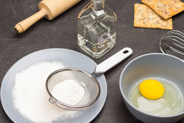 Flour and sieve on gray plate. Egg yolk in bowl.