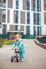 Cute little toddler girl in blue overalls riding on run balance bike. Happy healthy lovely baby child having fun with learning on leaner bicycle. Active kid on cold day outdoors.