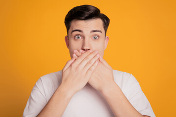 Portrait of scared man in white t-shirt cover mouth with hand on yellow background