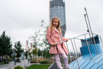 A cute little girl with a long, blond hair is having fun on a playground in the city park.
