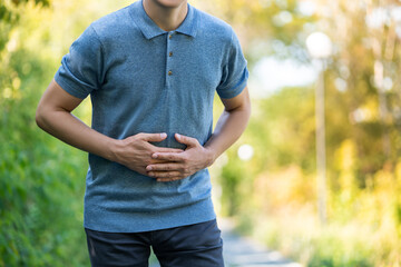 Abdominal pain when walking outdoors, man with stomach ache on nature background