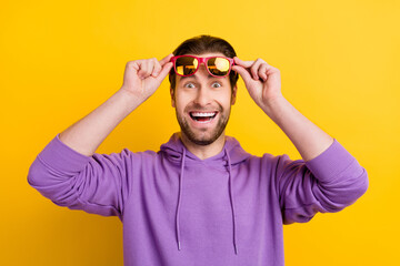 Photo of young excited man amazed shocked happy positive smile ahnds touch glasses isolated over yellow color background