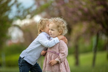 Fototapeta premium Beautiful children, toddler boy and girl, playing together in cherry blossom garden,boy giving a little bouquet of wild flowers to the girl. Kids friendship