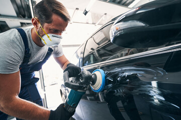 Repairman using polisher with blue pad on black automobile