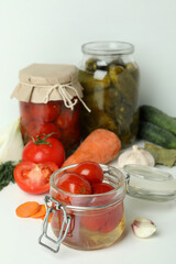 Jars of pickled vegetables and ingredients on white table