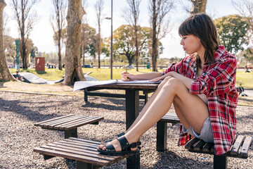 Medium shot of a beautiful woman sitting on a bench in the plaza, checking messages on her cell phone, smiling. Telecommunications, technology, internet concept.