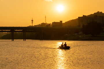 A man rowed on a lake stained with gold by the sunset