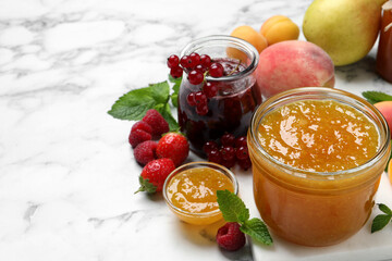 Jars with different jams and fresh fruits on white marble table. Space for text