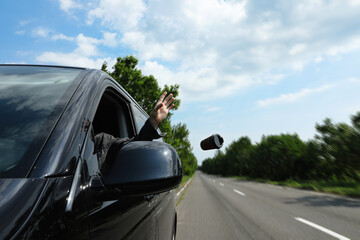 Fototapeta na wymiar Driver throwing away paper coffee cup from car window. Garbage on road