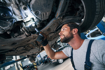 Automobile repairman examining car underside using flashlight - obrazy, fototapety, plakaty