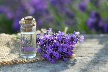Glass bottle of Lavender essential oil on wood table and flowers