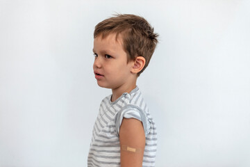 Sad Caucasian boy showing adhesive bandage on shoulder after getting vaccinated during COVID-19...