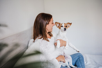 happy caucasian woman at home cuddling on bed with cute jack russell dog. Pets, love and relax at home