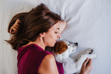 top view of young caucasian woman at home resting on bed with cute jack russell dog. Pets, love and relax