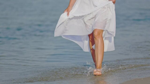 a woman in a white dress walks barefoot on the sea