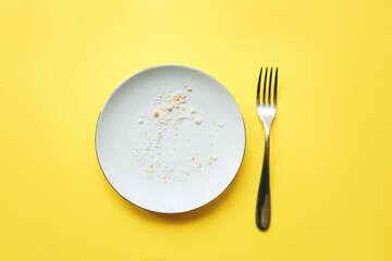 Conceptual image of the end of the holiday. Empty round plate with crumbs and fork on it on yellow...