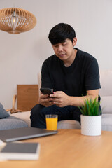 Living room concept a male young adult wearing black sitting on the cream sofa spending time with the smartphone in the living room