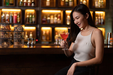 Nightlife concept a young woman in sexy outfits holding a glass of pink liquid enjoying its taste among the dim light in the bar
