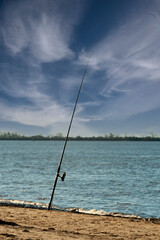 fishing rod on the shore of the desolate river with a sunny day