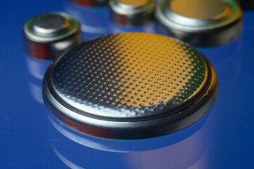 small button batteries of different sizes, highlighted in red and orange, lie against a blue background. close-up.