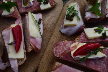 Brote mit Aufschnitt, Salami, Käse, Oliven, Kapern, Ruccula auf Holzbrettern für Jause, Brettlhause