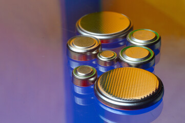 small button batteries of different sizes, highlighted in red and orange, lie against a blue background. close-up.