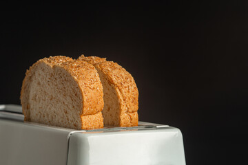 Rich and soft whole wheat bread in the toaster with a black background. Close-up photo. Space for...