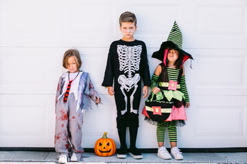 Children in Halloween costumes standing near wall and looking at camera