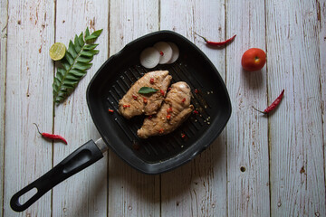 Top view of grilled chicken breast steak in a cooking pan along with condiments on a background.